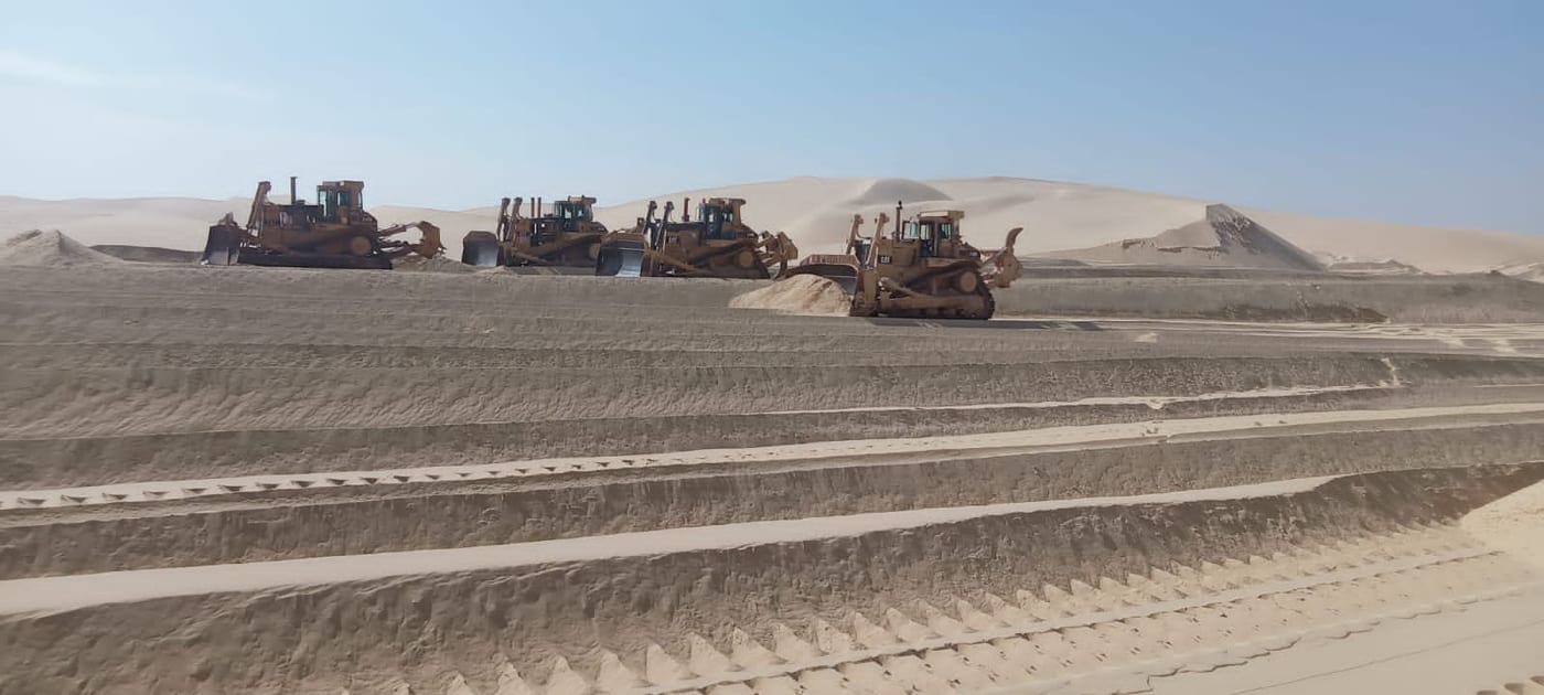 Bulldozers working together on sand dunes.