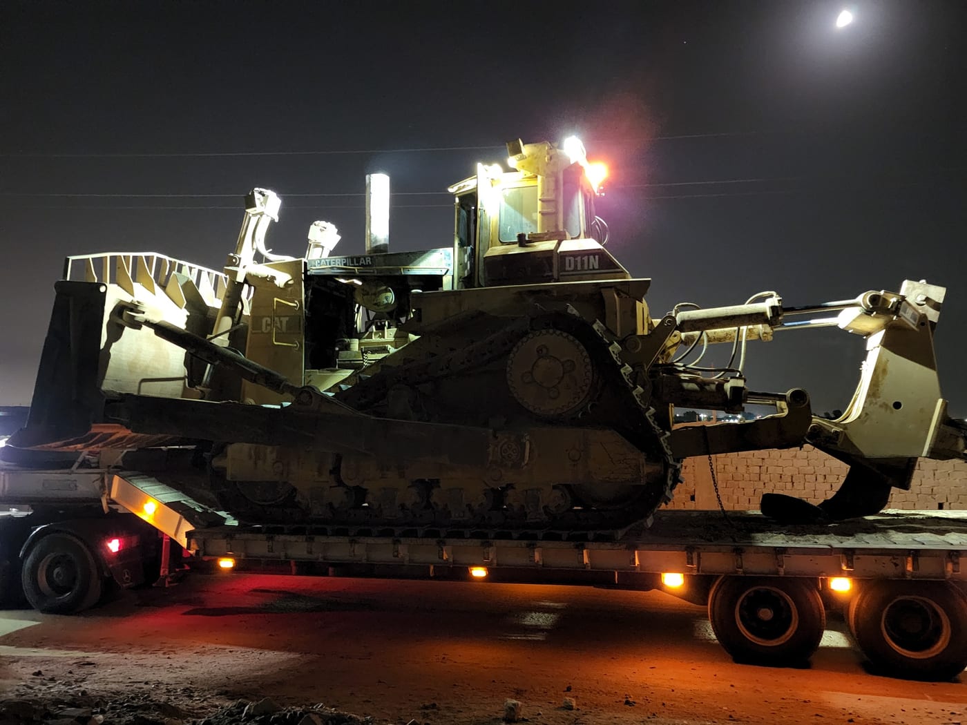 A bulldozer loaded on a lowbed trailer at night.