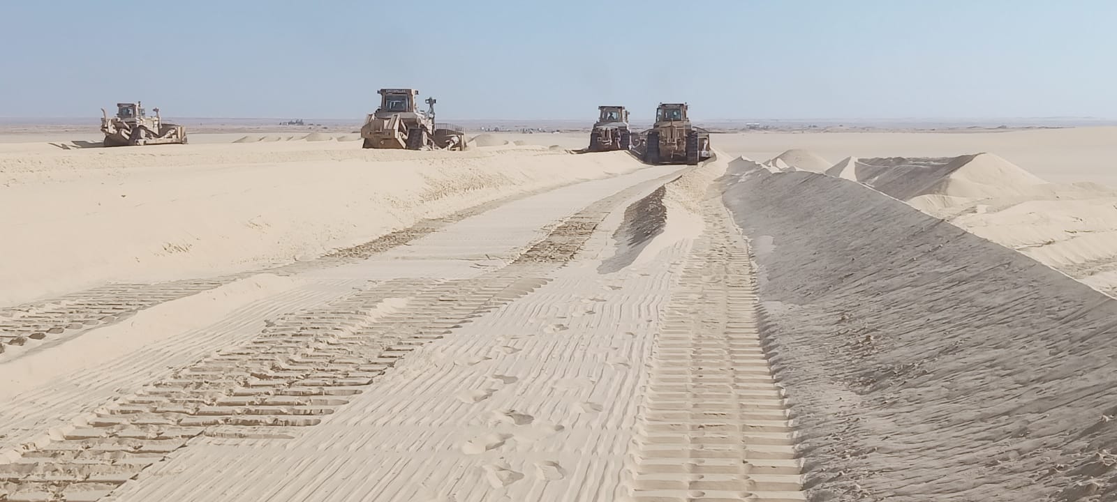 Bulldozers preparing a graded route through desert terrain.